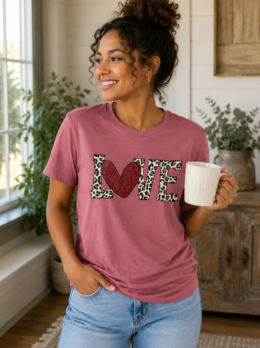 Woman wearing a bright pink graphic T-shirt featuring glitter-style XO letters and colorful hearts while smiling outdoors.