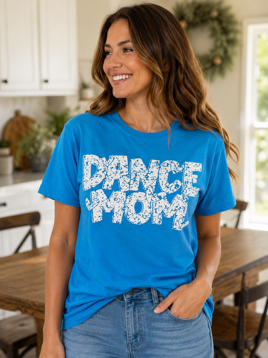 Woman wearing a royal blue T-shirt featuring a distressed white "Dance Mom" graphic while smiling indoors.