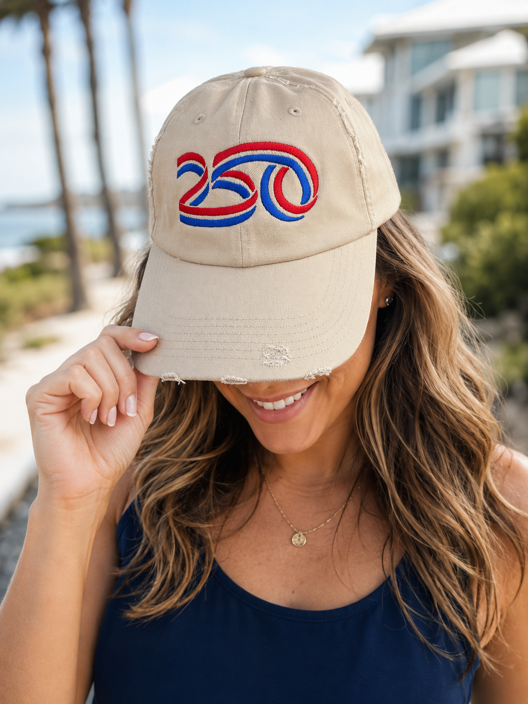 Beige distressed baseball cap featuring embroidered red, white, and blue "250" patriotic design on a woman outdoors, perfect for America's 250th anniversary celebrations.