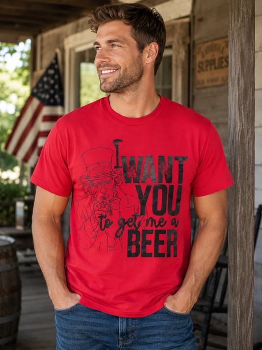 Man wearing a red graphic T-shirt featuring a distressed Uncle Sam design with the words "I Want You to Get Me a Beer," standing on a rustic porch with an American flag in the background.