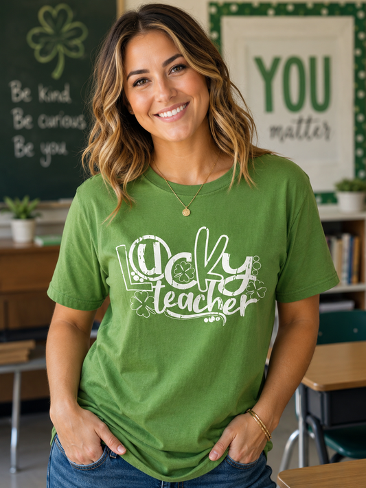 Woman wearing a green graphic T-shirt with a distressed white "Lucky Teacher" design and shamrocks while standing in a classroom decorated for St. Patrick's Day.