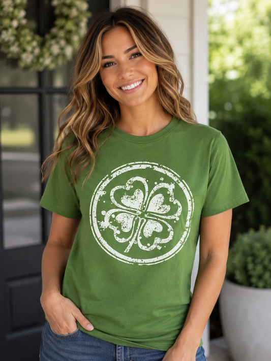 Woman wearing a green T-shirt featuring a distressed white four-leaf clover graphic inside a circular design while standing outdoors on a front porch.
